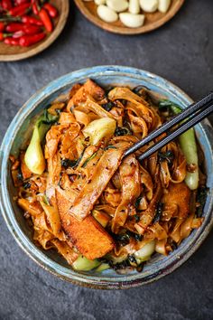 a bowl filled with noodles and vegetables next to chopsticks on a table top