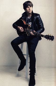 a man sitting on top of a stool with a guitar in his hand and wearing a leather jacket