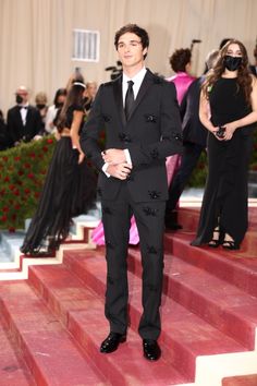 a young man in a tuxedo standing on steps with other people behind him