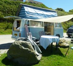 an old vw camper van is parked next to a picnic table and chairs