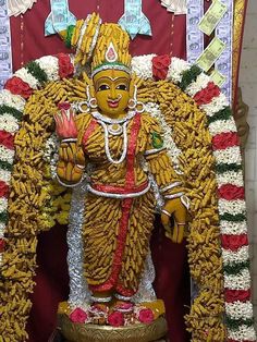 a statue of a god in front of a red and white wall with flowers on it