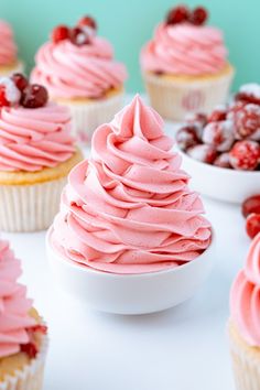 cupcakes with pink frosting and cherries in bowls on a white table