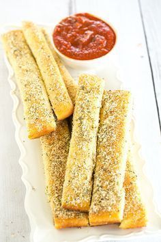 some bread sticks are on a plate with ketchup and sauce in the background