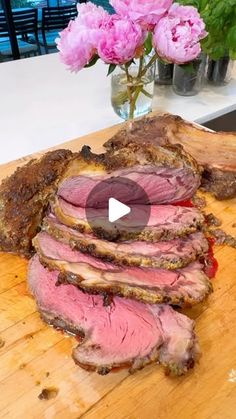 sliced meat sitting on top of a wooden cutting board next to pink carnations