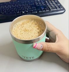 a woman's hand holding a cup of coffee in front of a computer keyboard