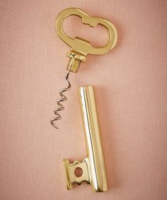 a golden key with a corkscrew attached to it sitting on a pink surface