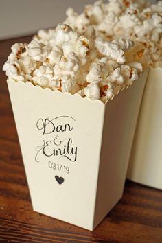 a box filled with white popcorn sitting on top of a wooden table next to a couple's initials