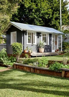 a small gray house sitting in the middle of a lush green yard with lots of trees