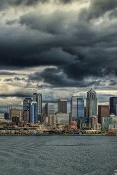 the city skyline is seen from across the water with storm clouds in the sky above