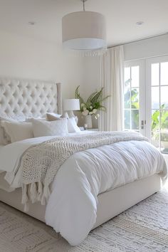 a large white bed sitting in a bedroom next to a window with curtains and pillows