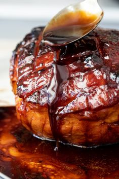 a spoon drizzling sauce on top of a piece of meat that is sitting on a plate