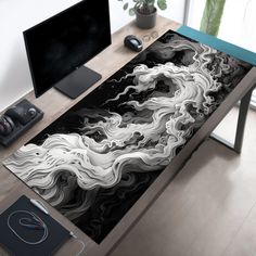 a computer desk with a black and white painting on the surface next to a monitor