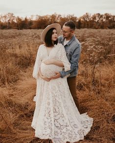 a pregnant woman in a white lace dress and cowboy hat standing next to her husband