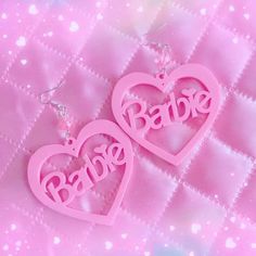 two pink heart shaped earrings with the word baby on them sitting on a pink background