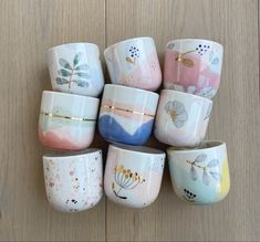 a bunch of cups that are sitting on a table together, all painted with different colors and designs