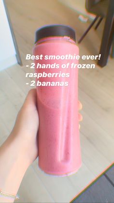 a person holding a pink smoothie in their hand