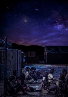 some people are sitting on the ground in front of a fence and looking up at the night sky