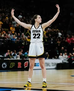 a female basketball player is standing on the court with her arms in the air and hands up