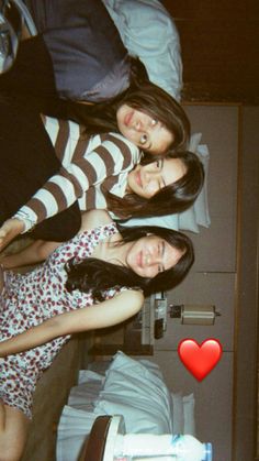 three young women standing next to each other in front of a bed with a red heart on it