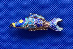 a blue and yellow fish broochle sitting on top of a blue cloth covered surface