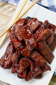 a plate full of meat with chopsticks next to it on a wooden table