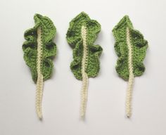 three crocheted leaves are shown on a white surface, one is green and the other is beige