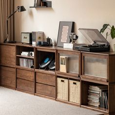 a record player sitting on top of a wooden book shelf next to a lamp and window