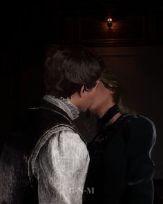 two people standing next to each other in front of a dark background, one kissing the other