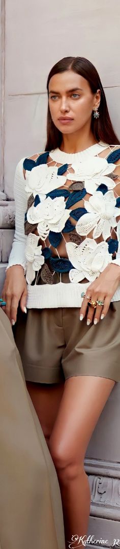 a woman sitting on the ground with her hands in her pockets and looking at the camera