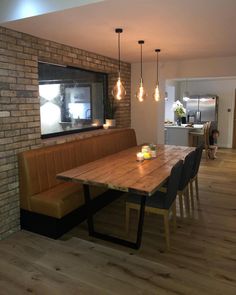 a dining room table and bench with lights hanging from the brick wall above it in front of a window