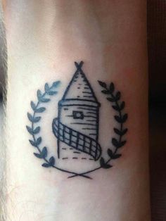 a small tattoo on the ankle of a person with a house and wreath around it