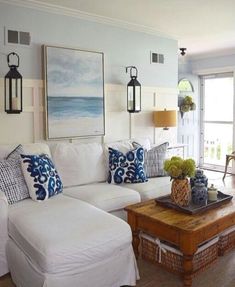 a living room with white couches and blue pillows on top of the sofas