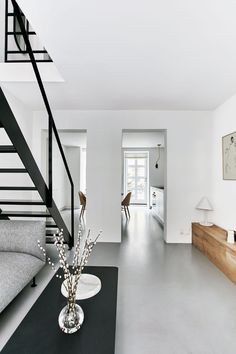 a living room with white walls and flooring next to a stair case in front of a gray couch