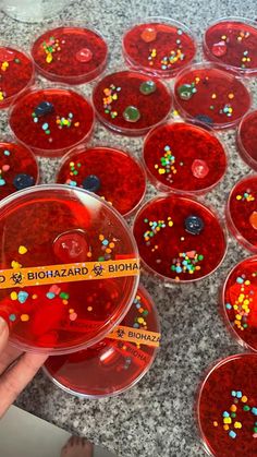 a hand holding a plastic container filled with red liquid and sprinkles