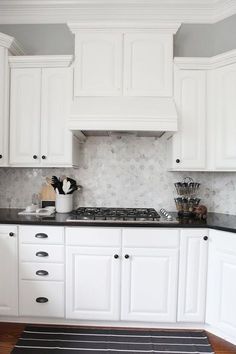 a kitchen with white cabinets and black counter tops, along with a striped rug on the floor