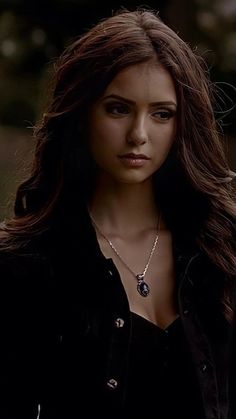 a woman with long brown hair wearing a black jacket and necklace on her neck is looking at the camera