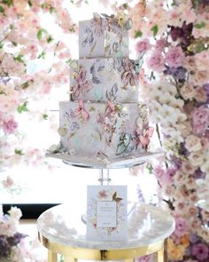 a three tiered cake on a table with flowers in the background