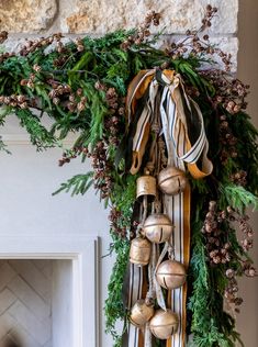 a christmas wreath with bells and pine cones hanging from it's front door, next to a fireplace