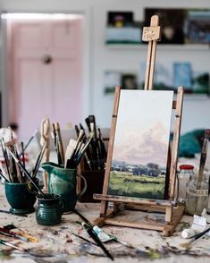 an easel with paint, brushes and other art supplies sitting on top of a table