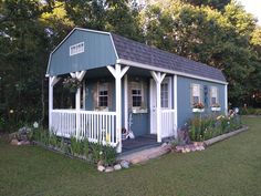 a small blue and white shed with flowers in the front yard