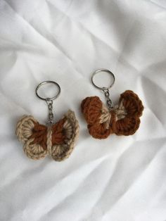 two crocheted keychains are sitting on a white sheet, one is brown and the other is tan