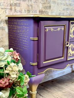 a purple cabinet with gold trim and writing on the doors is next to a potted plant