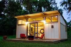 a small house with a deck and chairs in the yard at night, lit up by lights