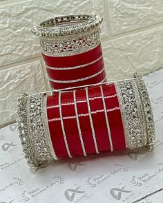 two red and silver bracelets sitting on top of a white table next to each other