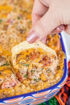 a hand dipping a tortilla chip into a casserole in a blue dish