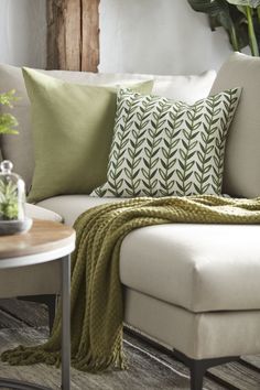 a white couch with green throw pillows and a blanket on it's back in a living room