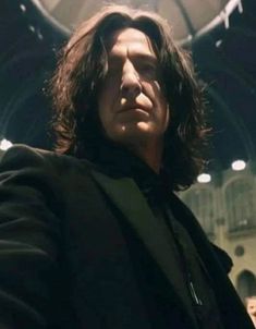 a man with long hair is holding his hand out in front of the camera while wearing a black suit