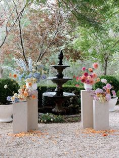 three vases with flowers are in front of a water fountain and some plants on the ground