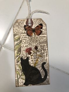 a tag with an image of a black cat and butterfly on it hanging from a string