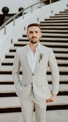 a man standing in front of some stairs wearing a white suit and flower boutonniere